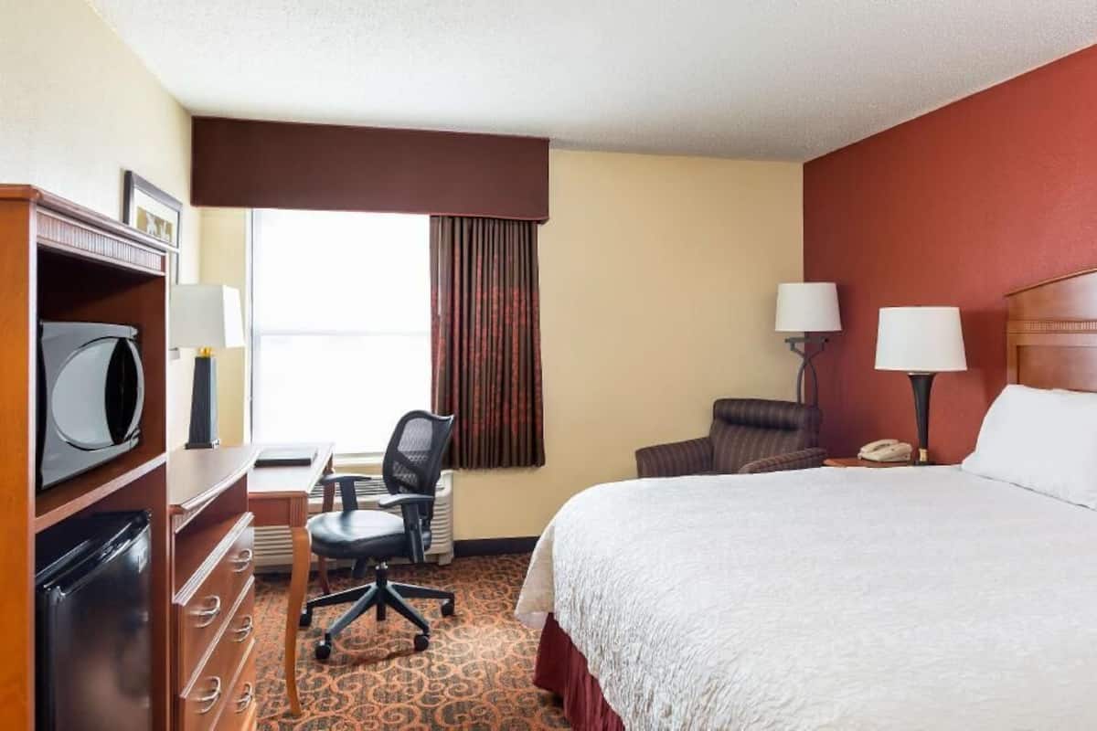 A hotel room with a bed, desk, chair, and a television.