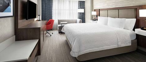 A hotel room with a large bed, a desk, a chair, a TV, and a window with curtains.