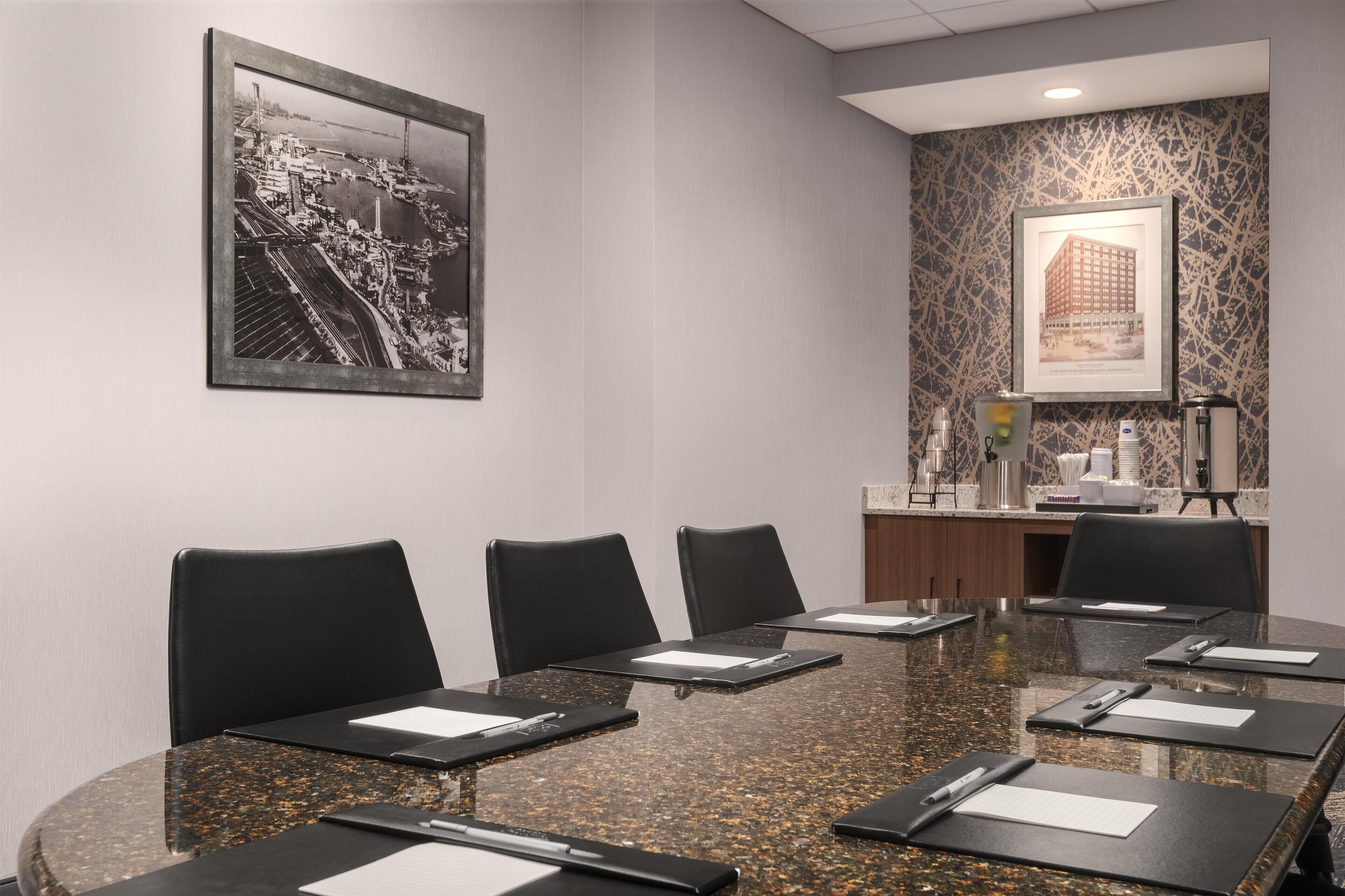 A conference room with a granite table, black chairs, and framed pictures on the walls.