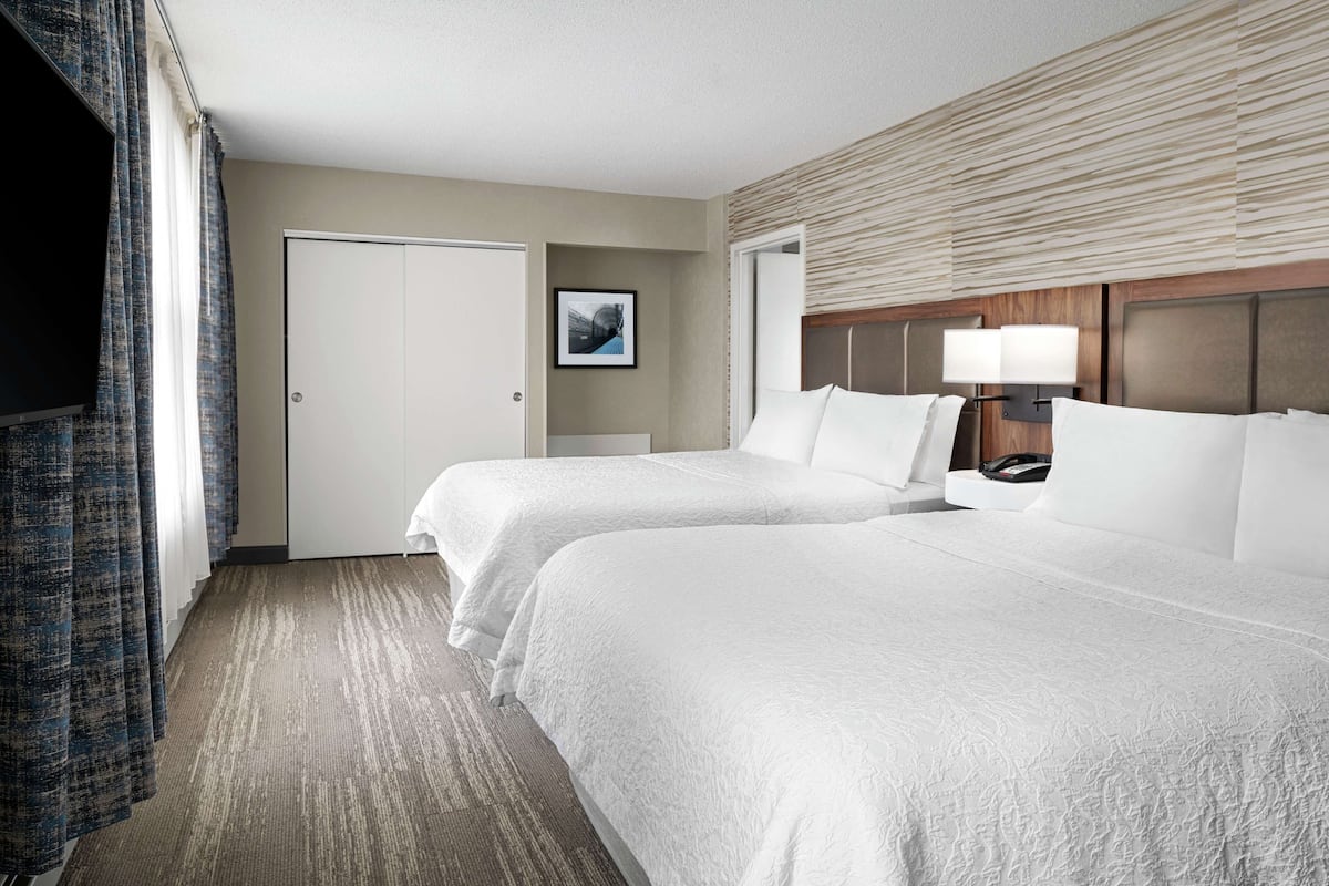 A hotel room with two beds, a flat-screen TV, a door, and a framed picture on the wall.