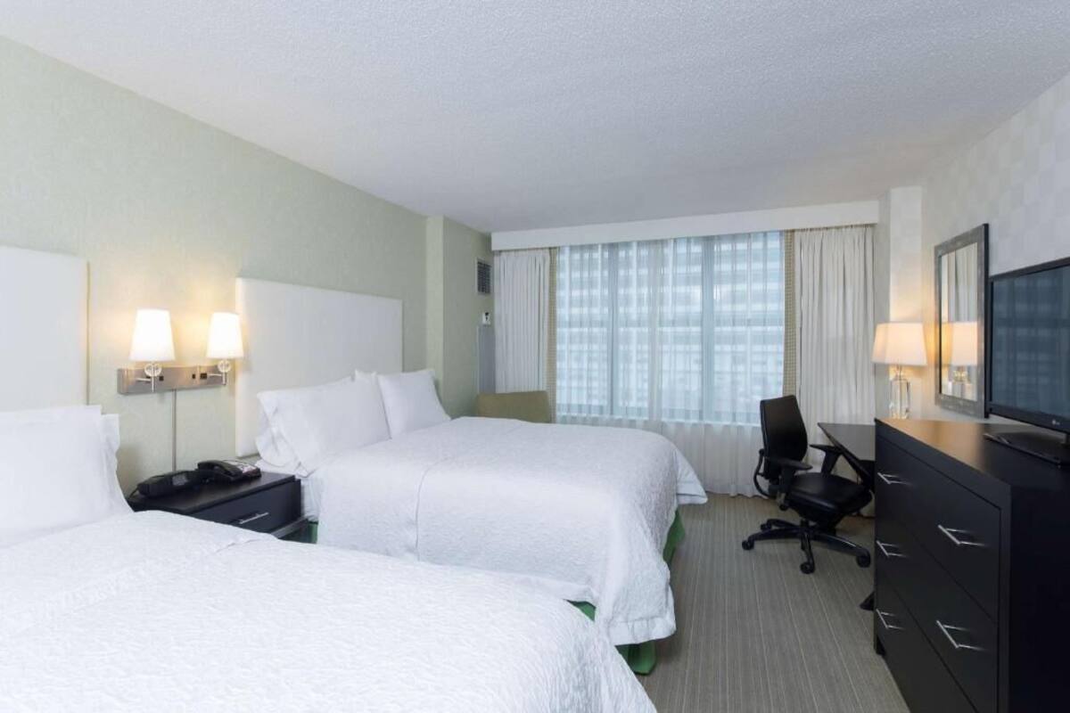 A hotel room with two beds, a desk with a computer, a chair, a TV, and a window with curtains.