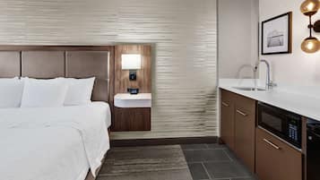 Quarto de hotel com cama, mesa de cabeceira com abajur, pia embutida e micro-ondas.