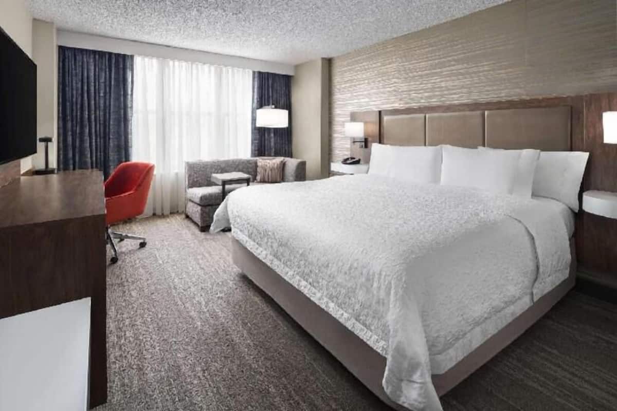A hotel room with a large bed, a desk, a chair, and a TV.