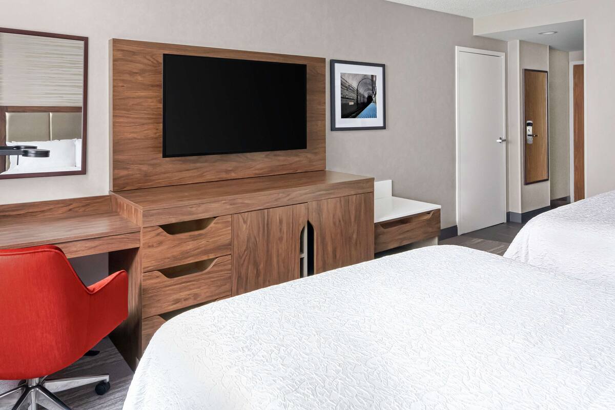 A hotel room with a large bed, a desk with a chair, a flat-screen TV, and a framed picture on the wall.