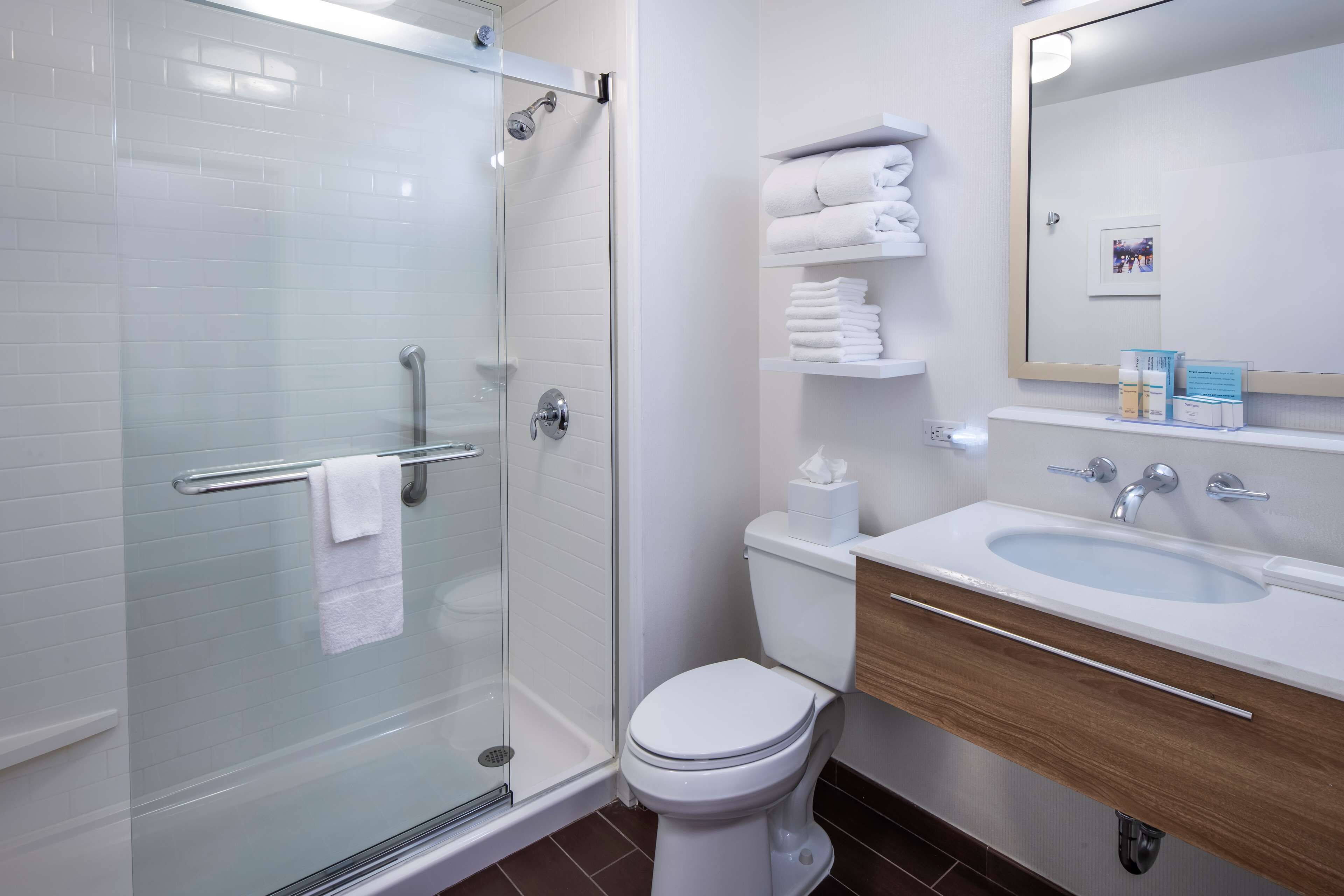 A modern bathroom with a glass-enclosed shower, a white toilet, and a sink with a wooden vanity.