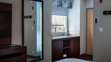 Habitación de hotel con un espejo grande, un tocador de madera con lavamanos, una cama y vistas al exterior a través de una ventana.
