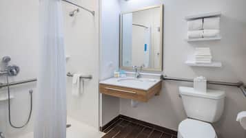 A bathroom with a shower, sink, toilet, and towel racks.