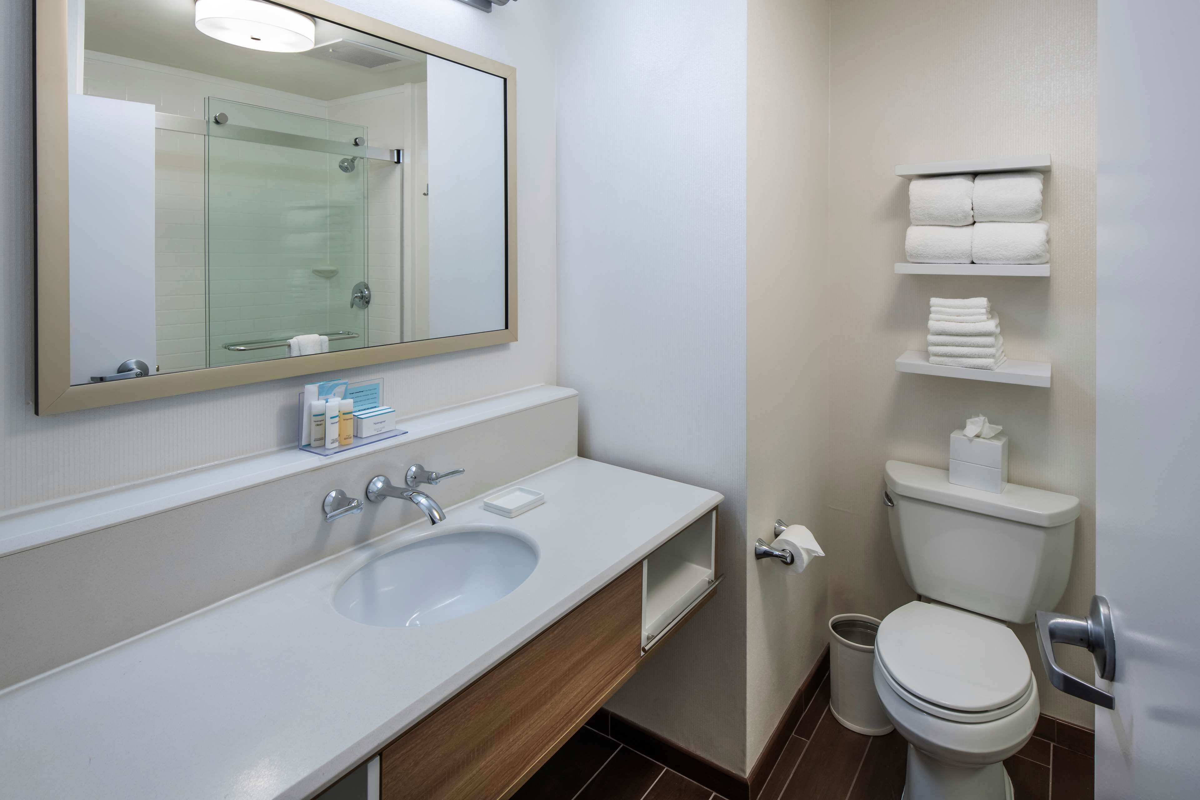 Une salle de bain moderne avec un grand miroir, un lavabo, des toilettes et des étagères où sont rangées les serviettes.