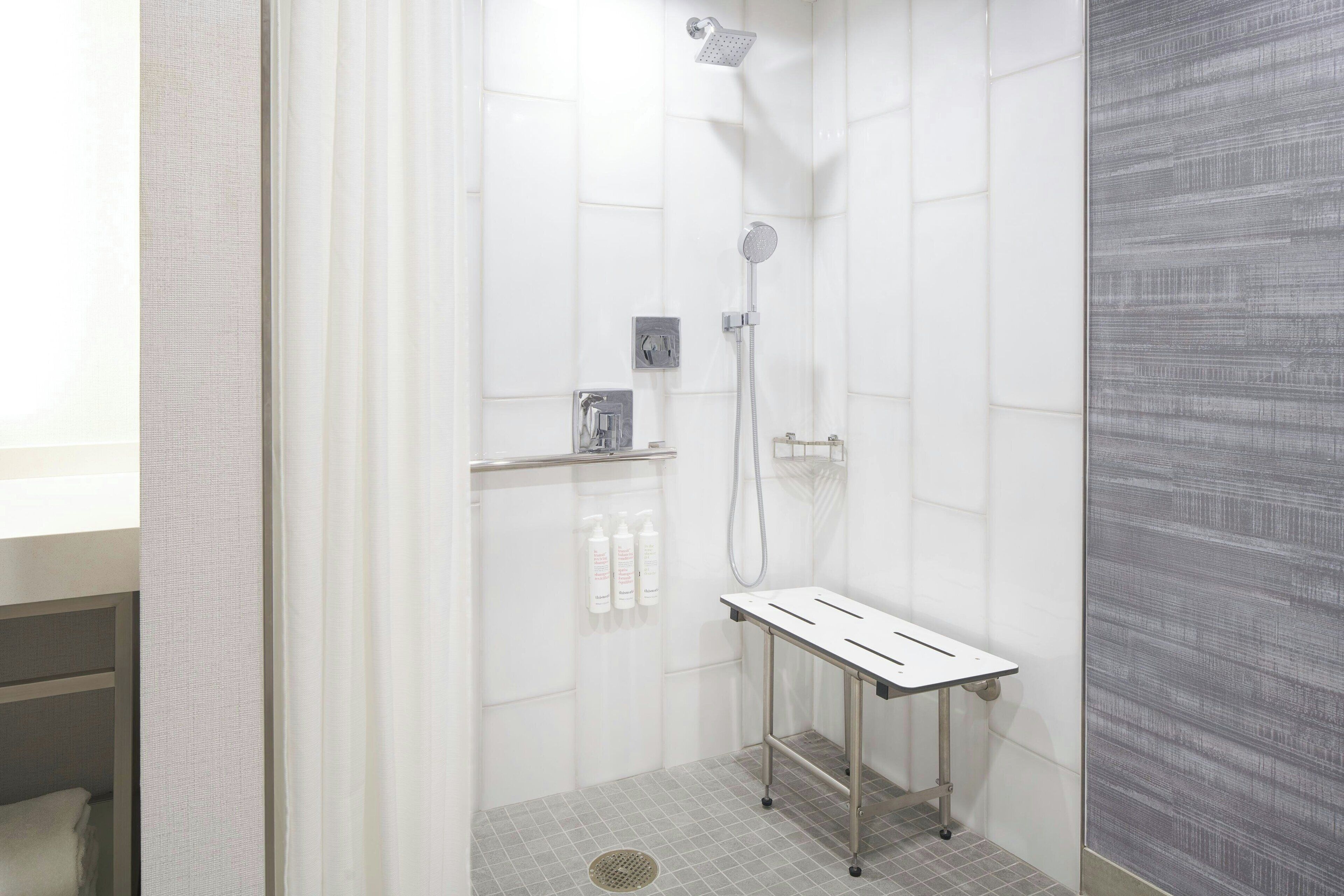 Eine moderne Dusche mit Handbrause, Wandarmatur und einer kleinen Ablage für Toilettenartikel.