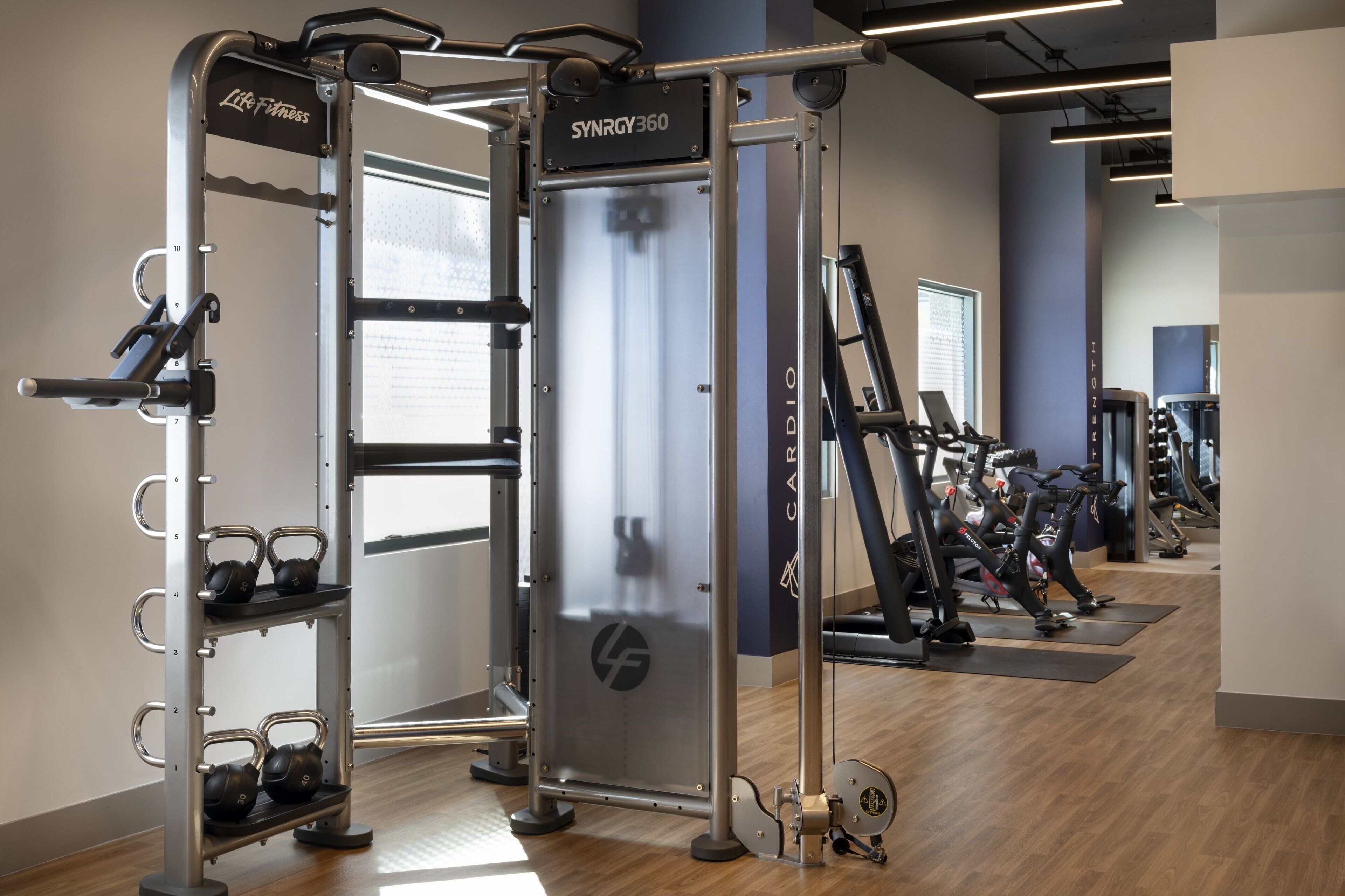 A gym with a weightlifting station, cardio machines, and kettlebells.