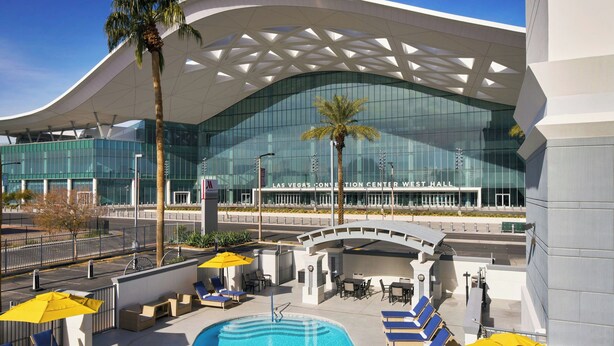 A pool area with lounge chairs and umbrellas, a palm tree, and a modern building with a glass facade in the background. - Las Vegas Marriott (Las Vegas)