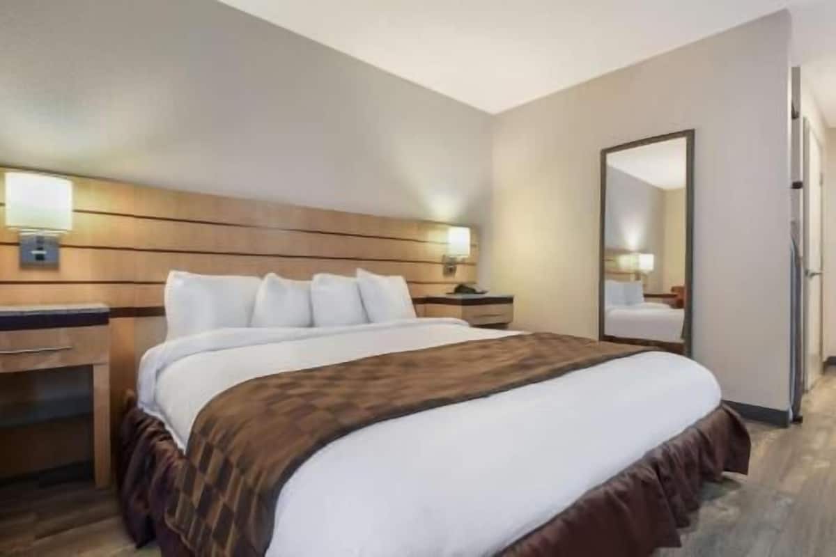 Una habitación de hotel con una cama grande, cabecero de madera, mesitas de noche y un espejo.