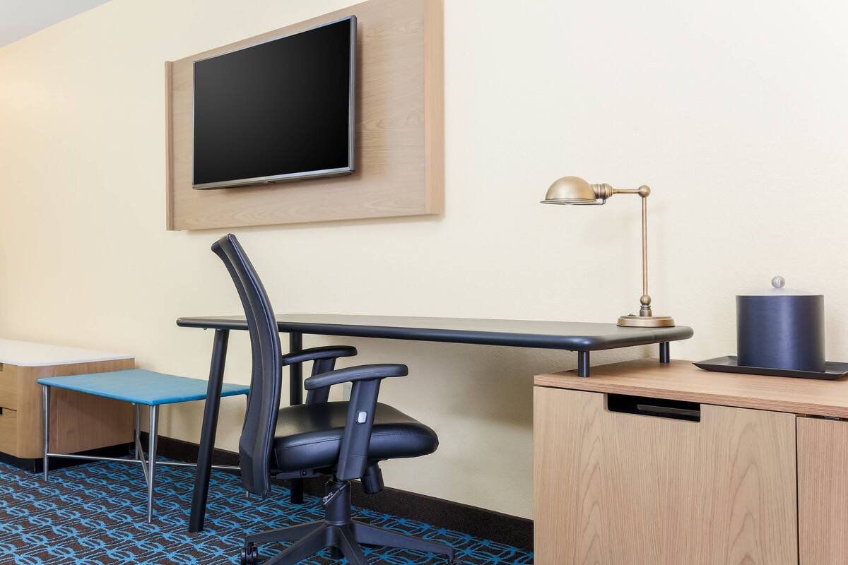 Une chambre d’hôtel équipée d’un bureau, d’une chaise, d’une télévision, d’une lampe et d’un petit placard.