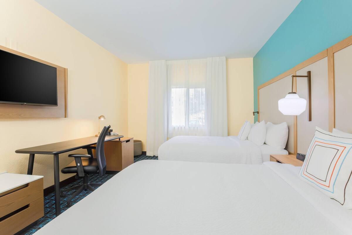 Une chambre d’hôtel comprenant un lit, un bureau avec une chaise, un téléviseur fixé au mur et une fenêtre avec des rideaux.