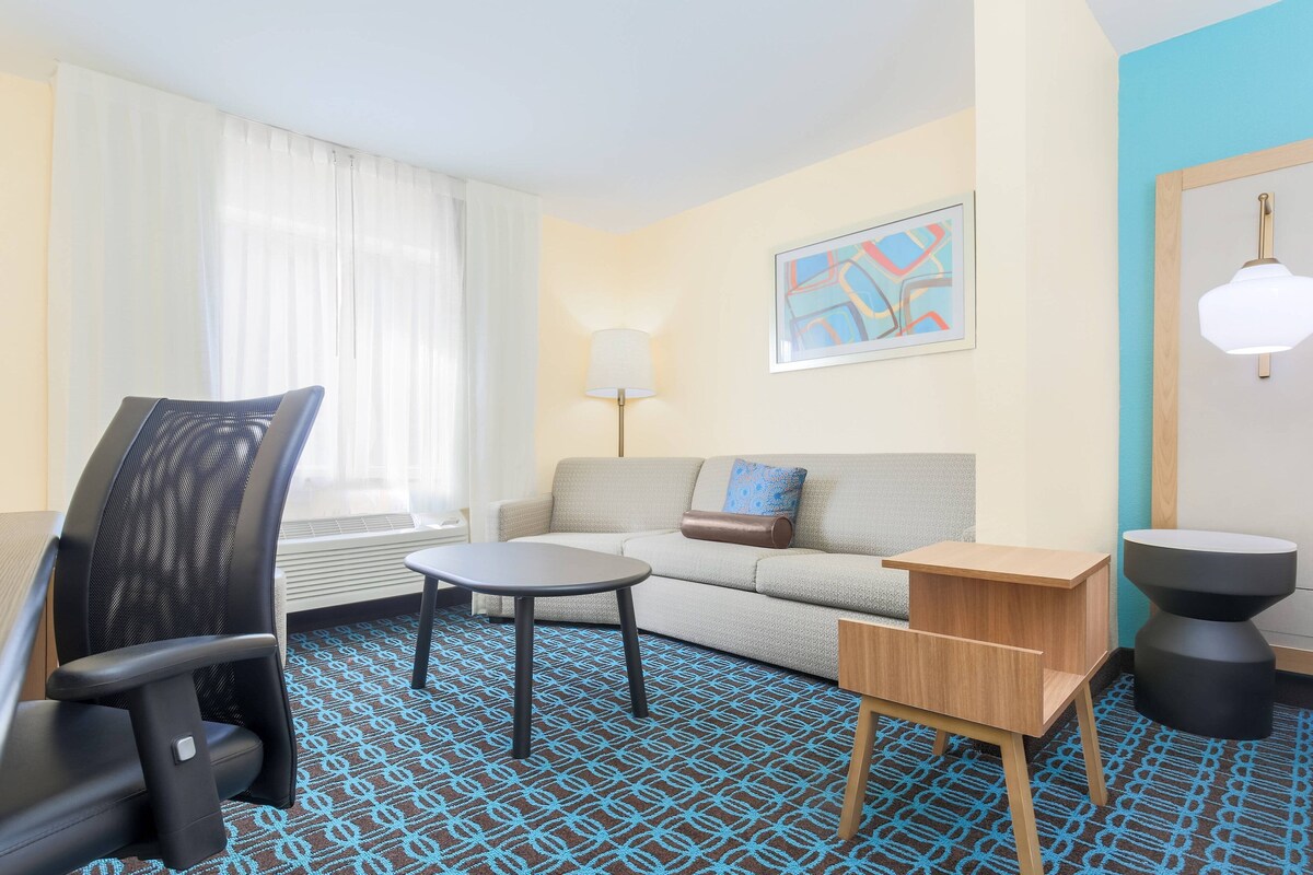 Une chambre d’hôtel équipée d’un canapé, d’un fauteuil, d’une petite table, d’une lampe et d’un élément décoratif mural.
