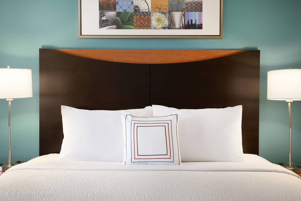 Un lit bien fait, avec une couette blanche et deux oreillers, dont l’un présente un motif géométrique.