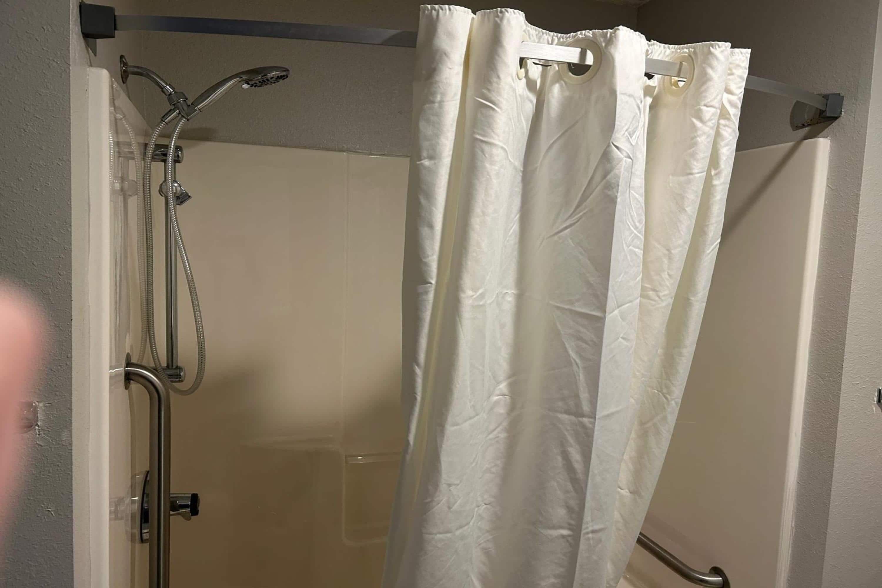 A shower area with a white curtain, a handheld showerhead, and a wall-mounted faucet.