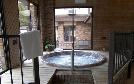 A hot tub on a wooden deck with a brick wall and a window in the background.