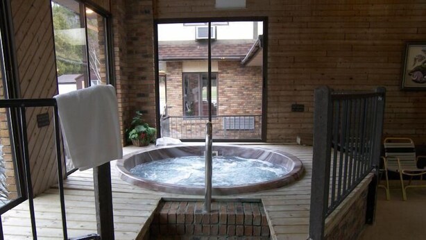 Un bain à remous sur une terrasse en bois, avec un mur en briques et une fenêtre en arrière-plan.