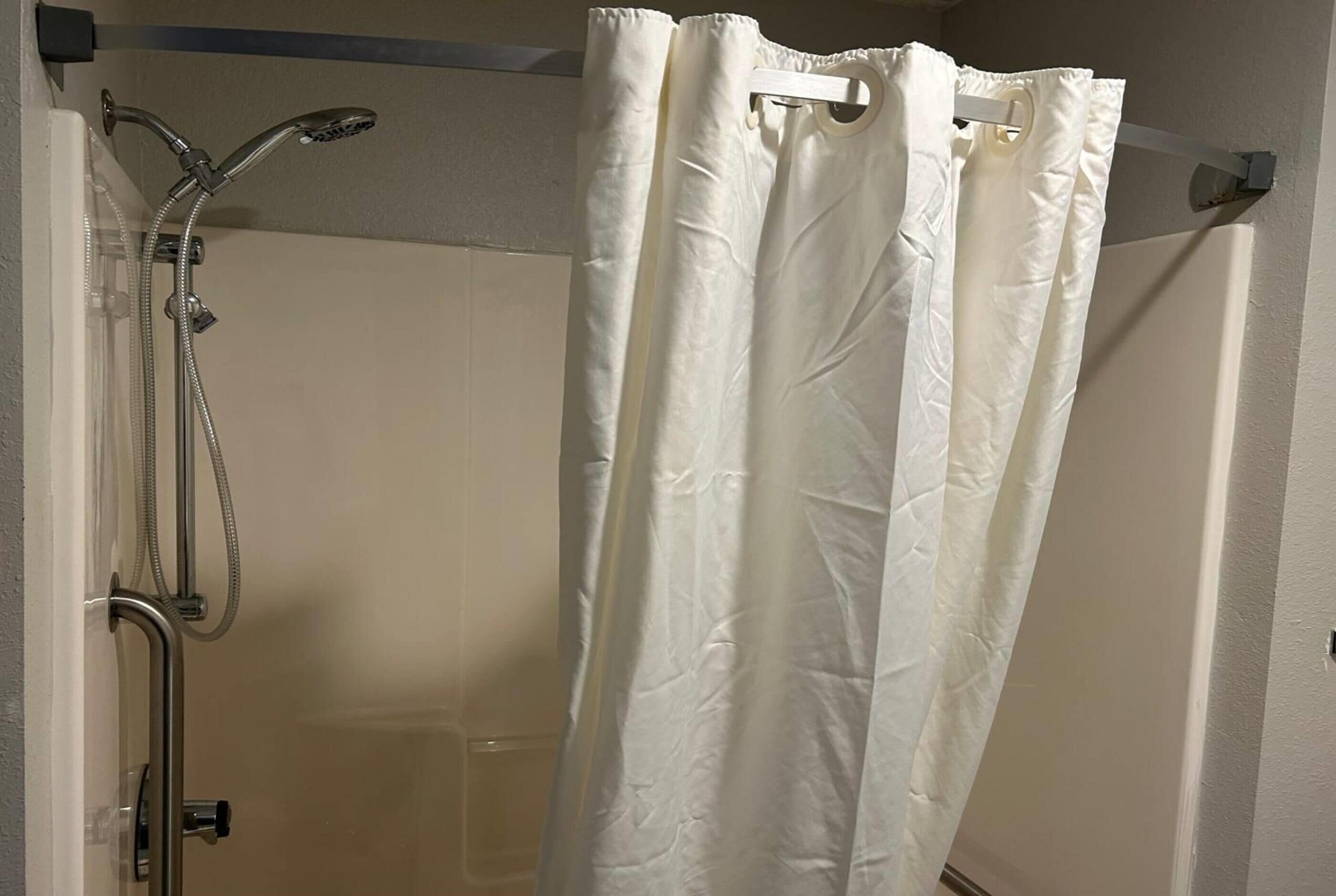 Eine Dusche mit weißem Vorhang, einer Handbrause und einem wandmontierten Wasserhahn.