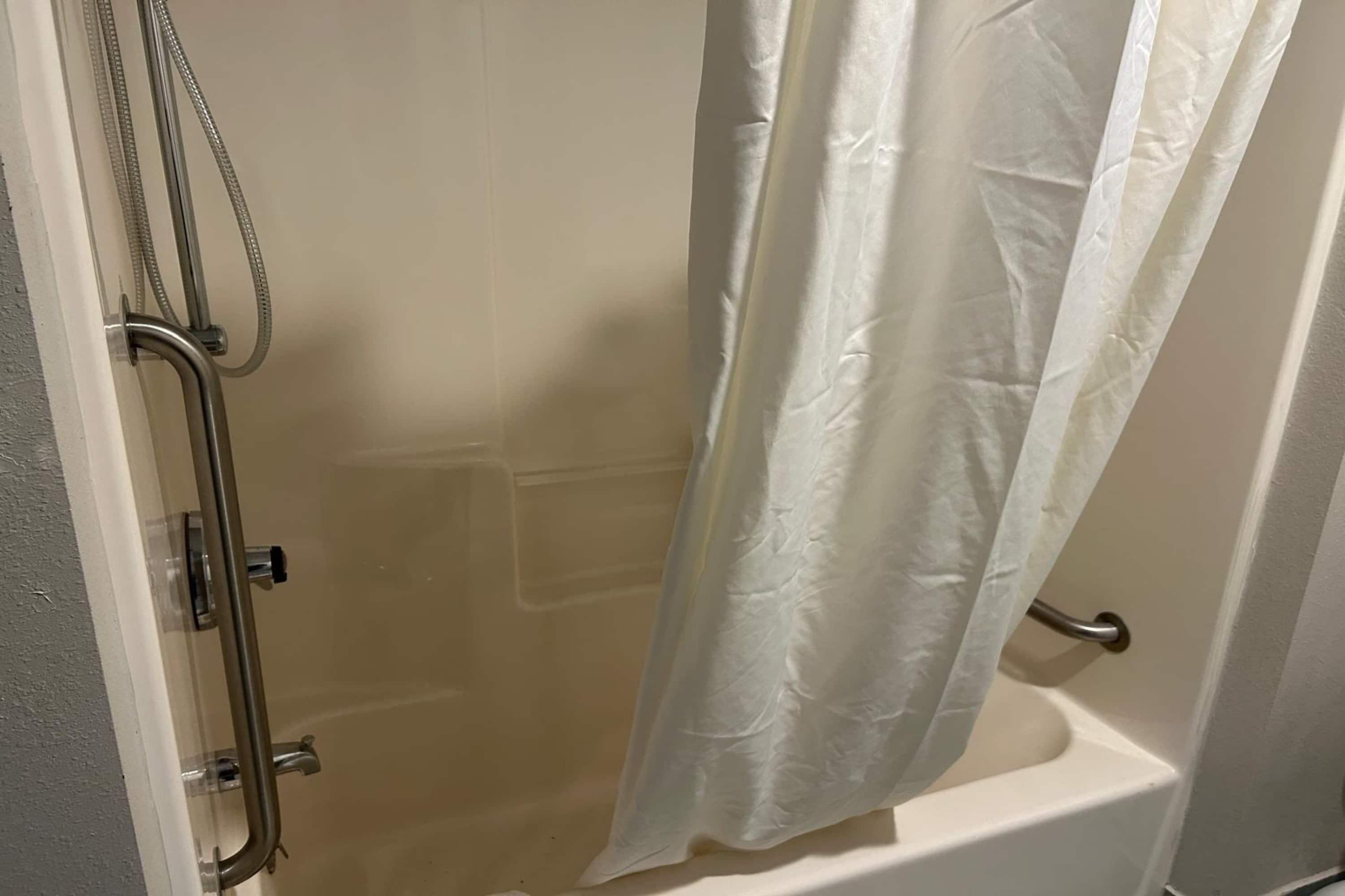 Un área de ducha con puerta de vidrio, ducha y cortina blanca.