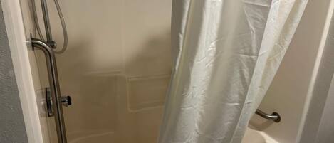 Un área de ducha con puerta de vidrio, ducha y cortina blanca.
