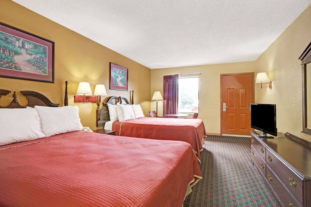 A hotel room with two beds, a television, a dresser, and a window with curtains.