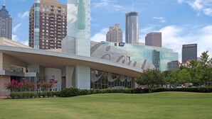 A modern building with a glass facade and a Coca-Cola logo, surrounded by a well-maintained lawn and other high-rise buildings in the background. - Travelodge by Wyndham Forest Park Atlanta South (Forest Park)