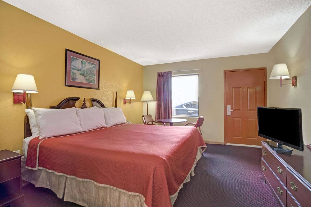 A hotel room with a large bed, two bedside lamps, a television, a small table, and a window with curtains.