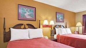 A hotel room with two beds, each with a wooden headboard and red bedding. There are two wall-mounted lamps and framed pictures above the beds. - Travelodge by Wyndham Forest Park Atlanta South (Forest Park)
