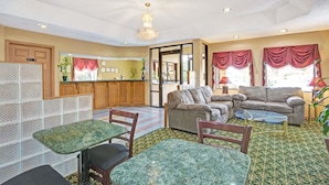 A spacious living area with a sofa set, a dining table, and chairs. There is a kitchen area in the background with wooden cabinets and a refrigerator. - Travelodge by Wyndham Forest Park Atlanta South (Forest Park)