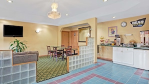 A hotel room with a dining area, a TV mounted on the wall, a clock, and a sign that reads "BEAR OLEO". - Travelodge by Wyndham Forest Park Atlanta South (Forest Park)