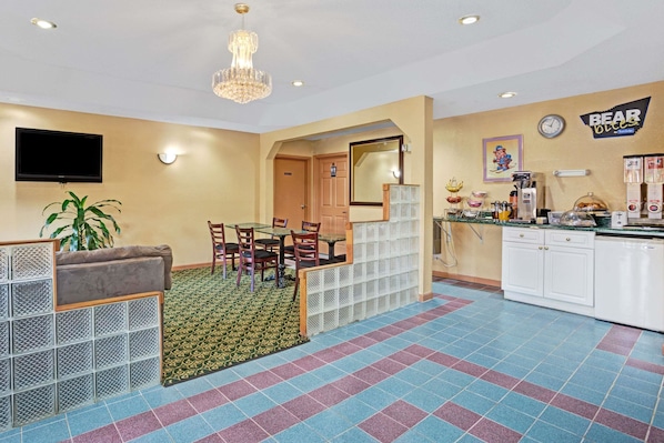 A hotel room with a dining area, a TV mounted on the wall, a clock, and a sign that reads "BEAR OLEO".