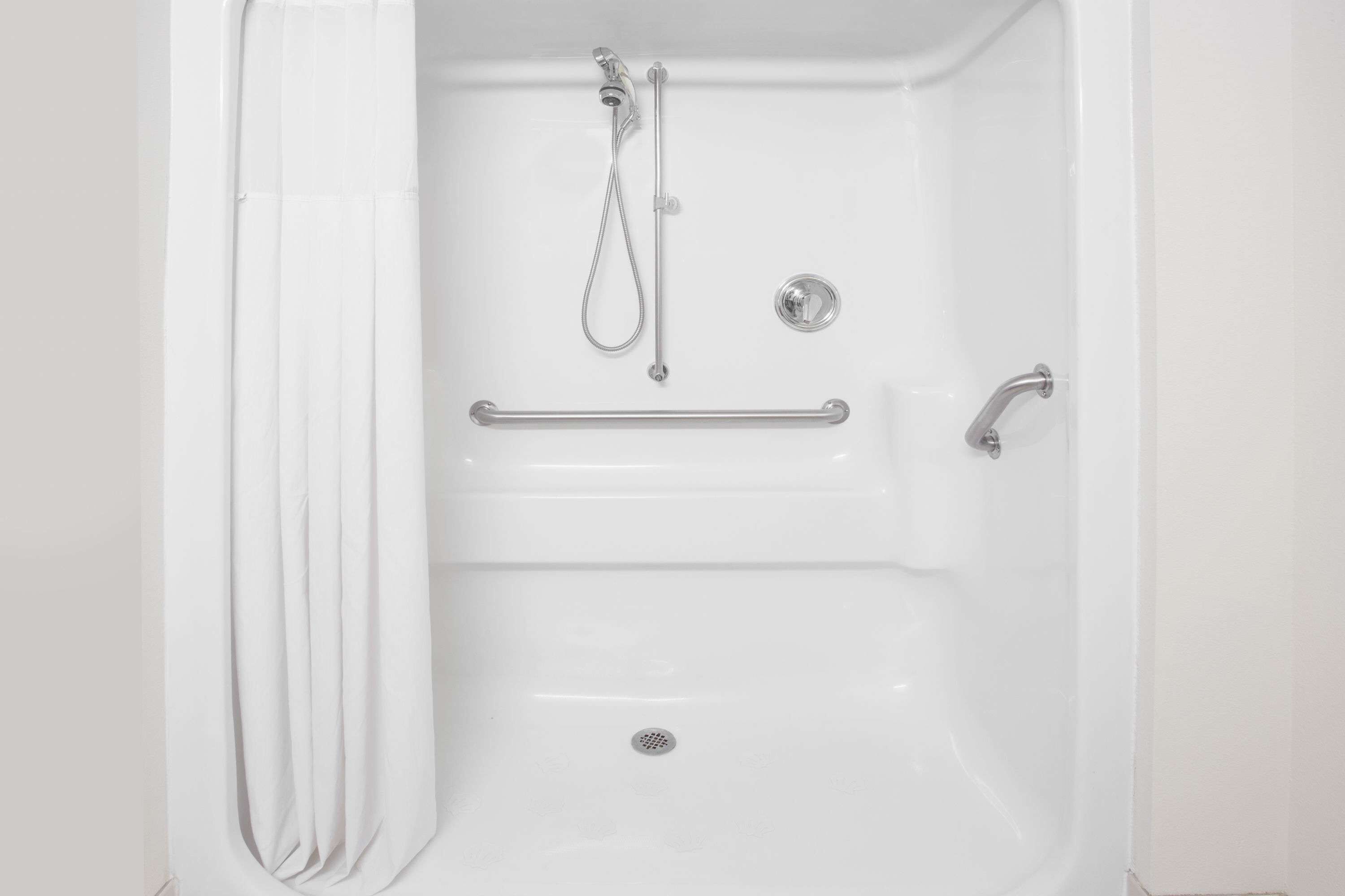 A white bathtub with a handheld showerhead, a grab bar, and a faucet.