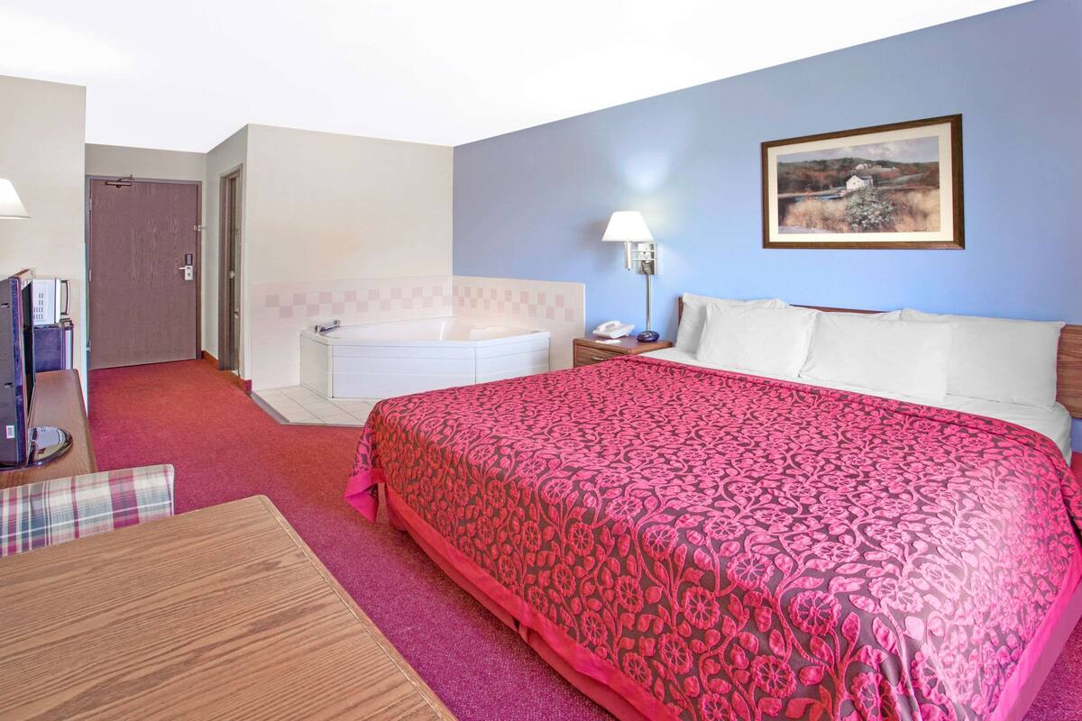 A hotel room with a large bed, a bathroom, a dining area, and a painting on the wall.
