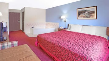 A hotel room with a large bed, a bathroom, a dining area, and a painting on the wall.