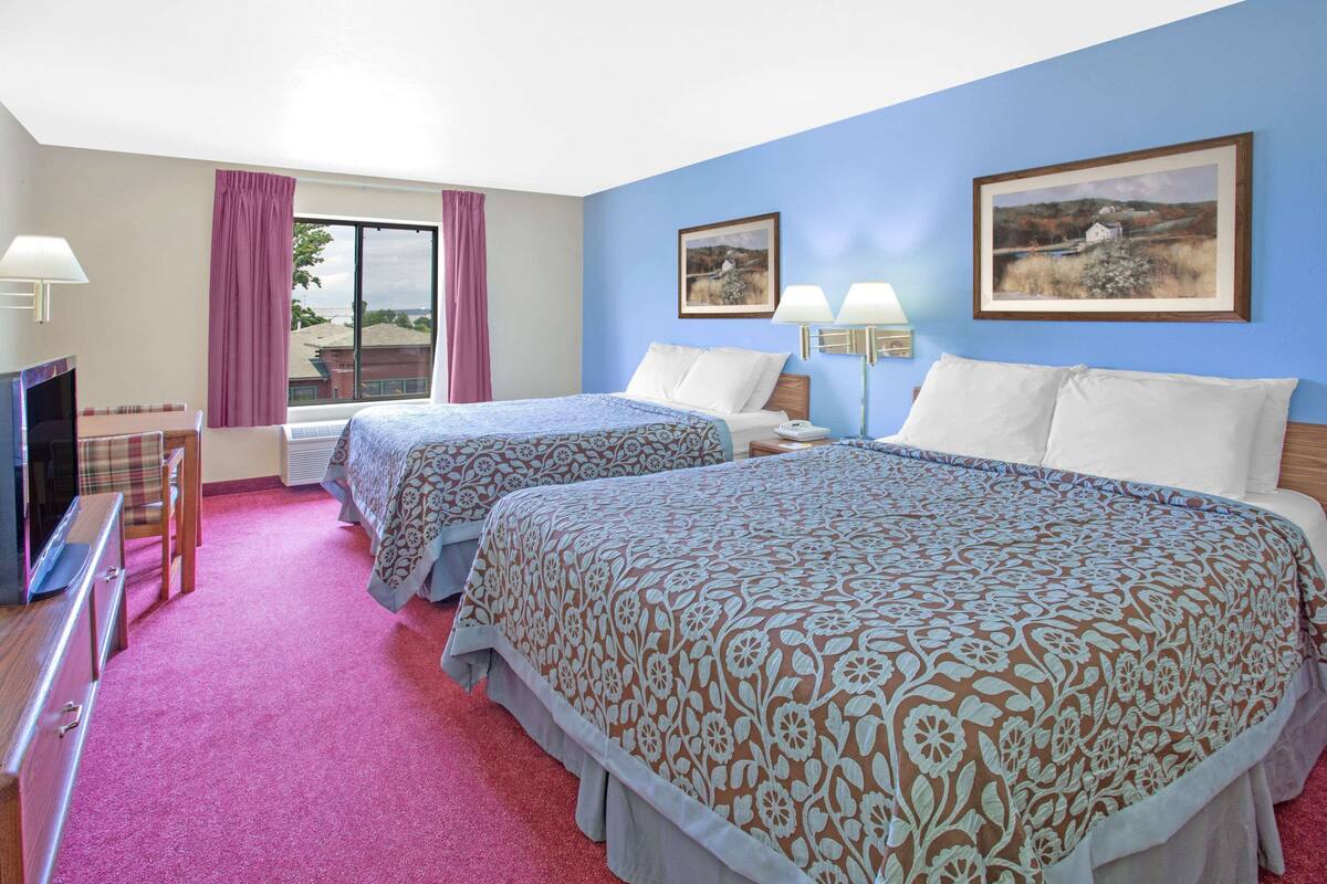 A hotel room with two beds, a TV, a desk, and a window with curtains.