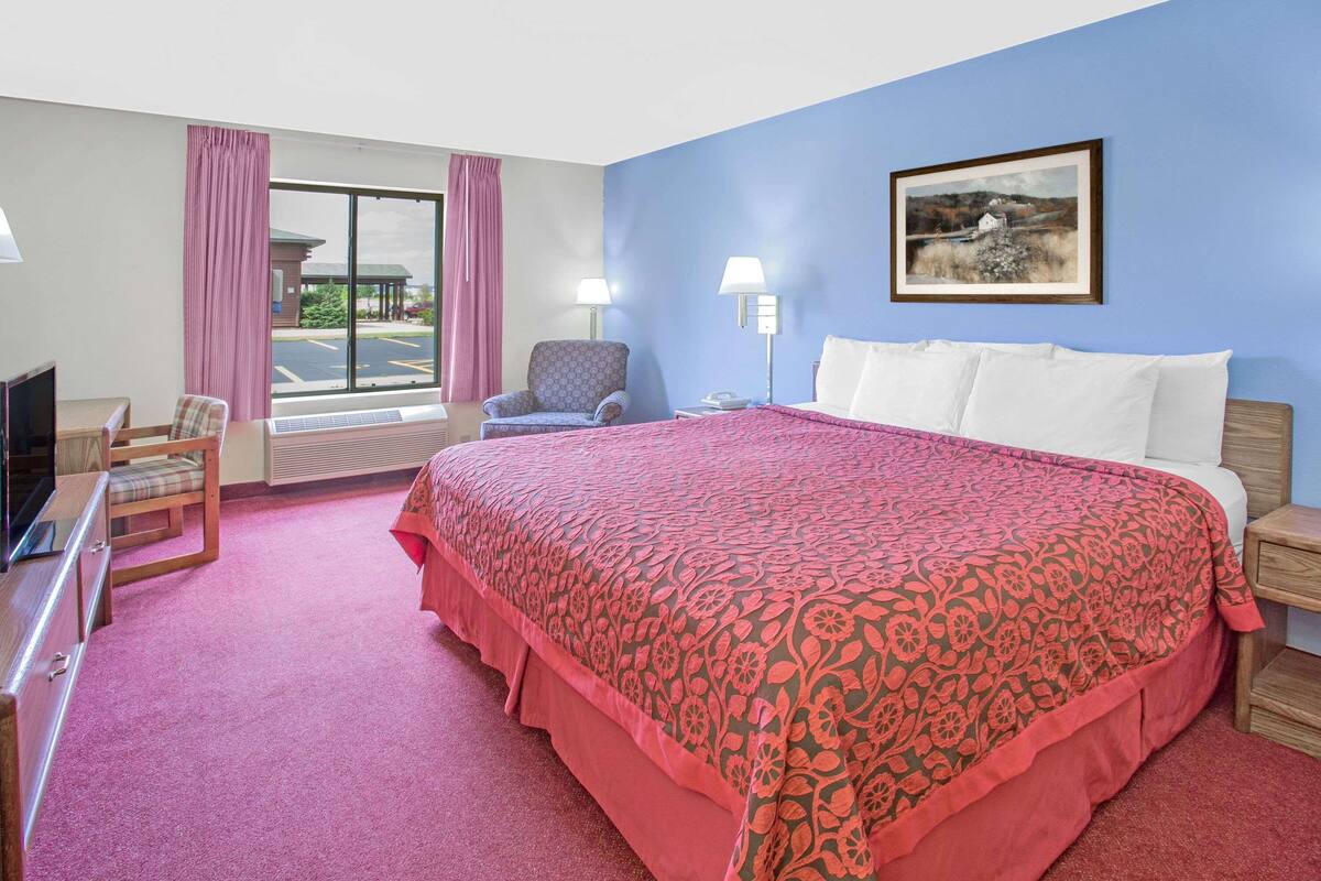 A hotel room with a large bed, a chair, a desk with a computer, and a window with curtains.