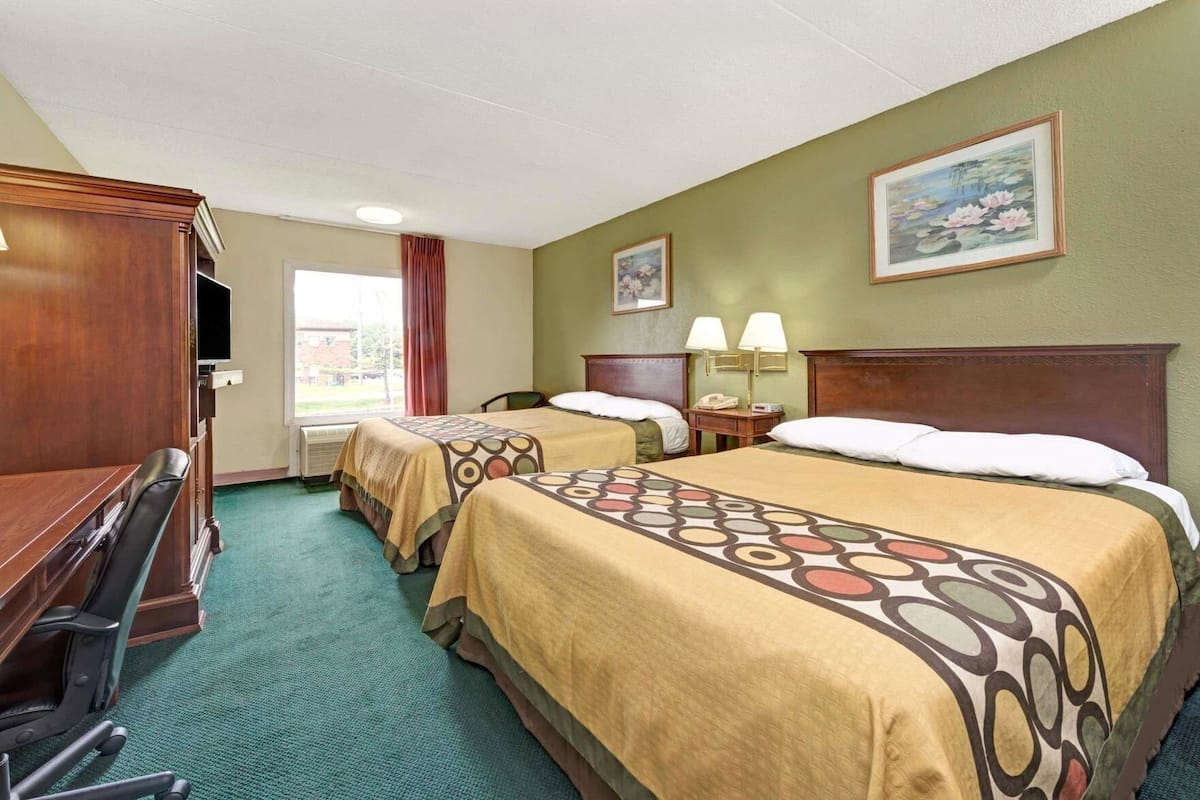 A hotel room with two beds, a desk, a chair, a TV, and a painting on the wall.