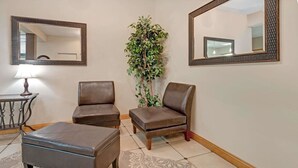 A room with two leather armchairs, a small ottoman, a potted plant, and two wall-mounted mirrors.
