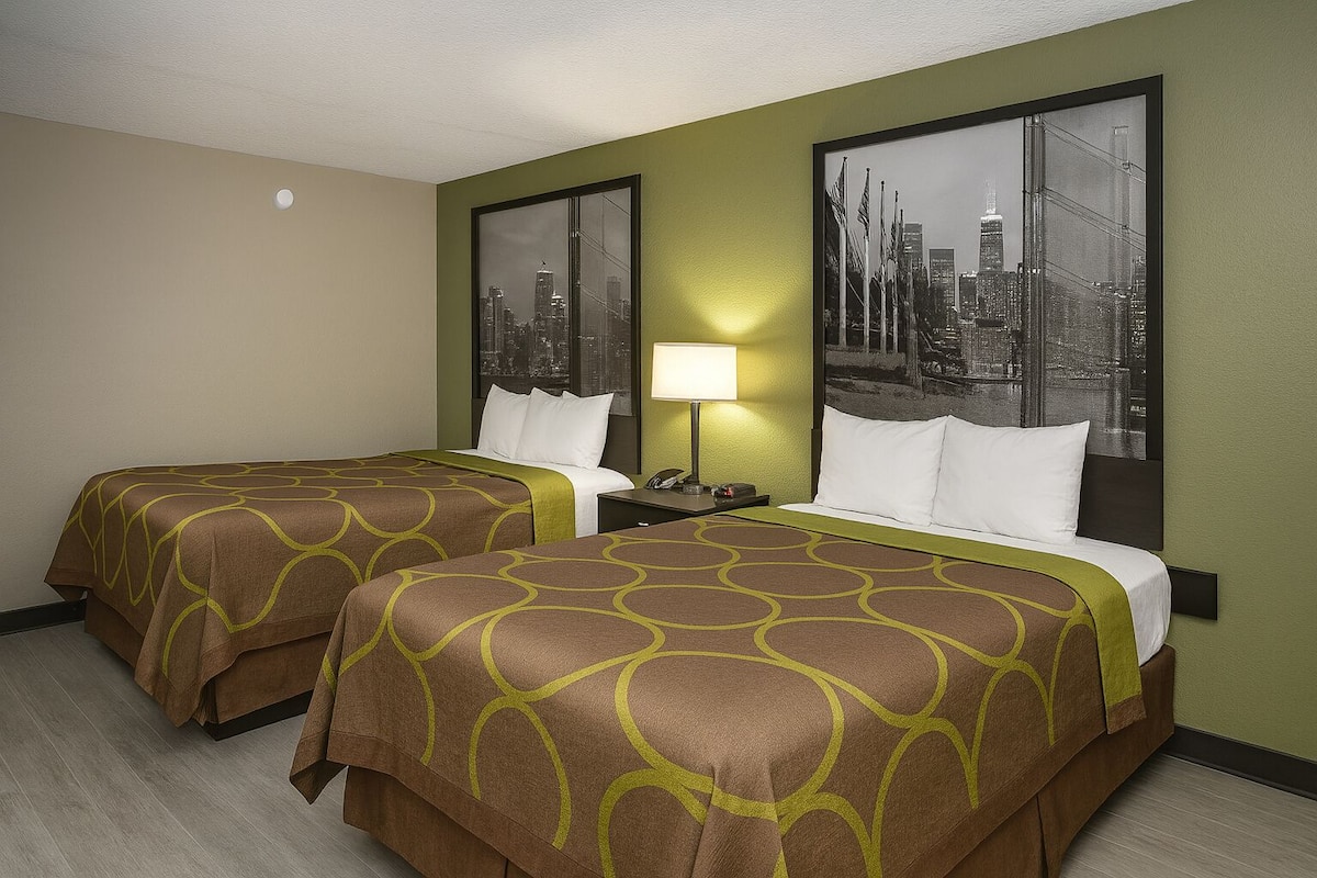 A hotel room with two beds, a cityscape view, a lamp, and a nightstand.