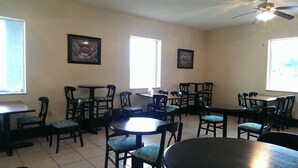 A dining area with multiple tables and chairs, ceiling fans, and framed artwork on the walls.