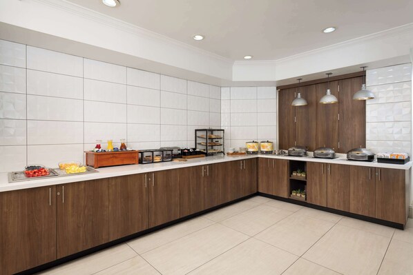 Una cocina moderna con una isla grande, paredes de azulejos blancos, armarios de madera e iluminación colgante.