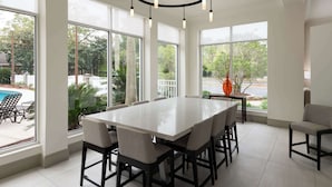 A spacious dining area with a large table and chairs, large windows offering views of the outdoors, and a modern chandelier. - Hilton Garden Inn Tallahassee (Tallahassee)