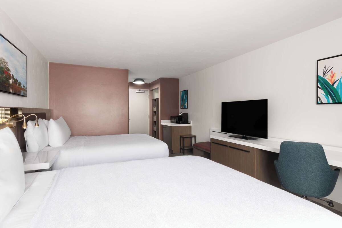 A hotel room with two beds, a desk, a television, and a chair.