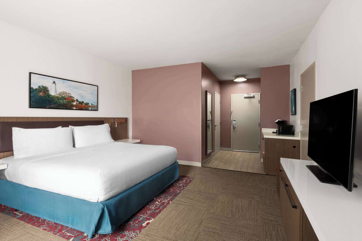 A hotel room with a bed, a television, a desk, and a bathroom.