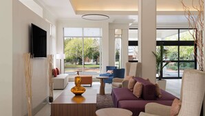 A modern living room with a flat-screen TV, comfortable seating, and large windows offering a view of the outdoors. - Hilton Garden Inn Tallahassee (Tallahassee)