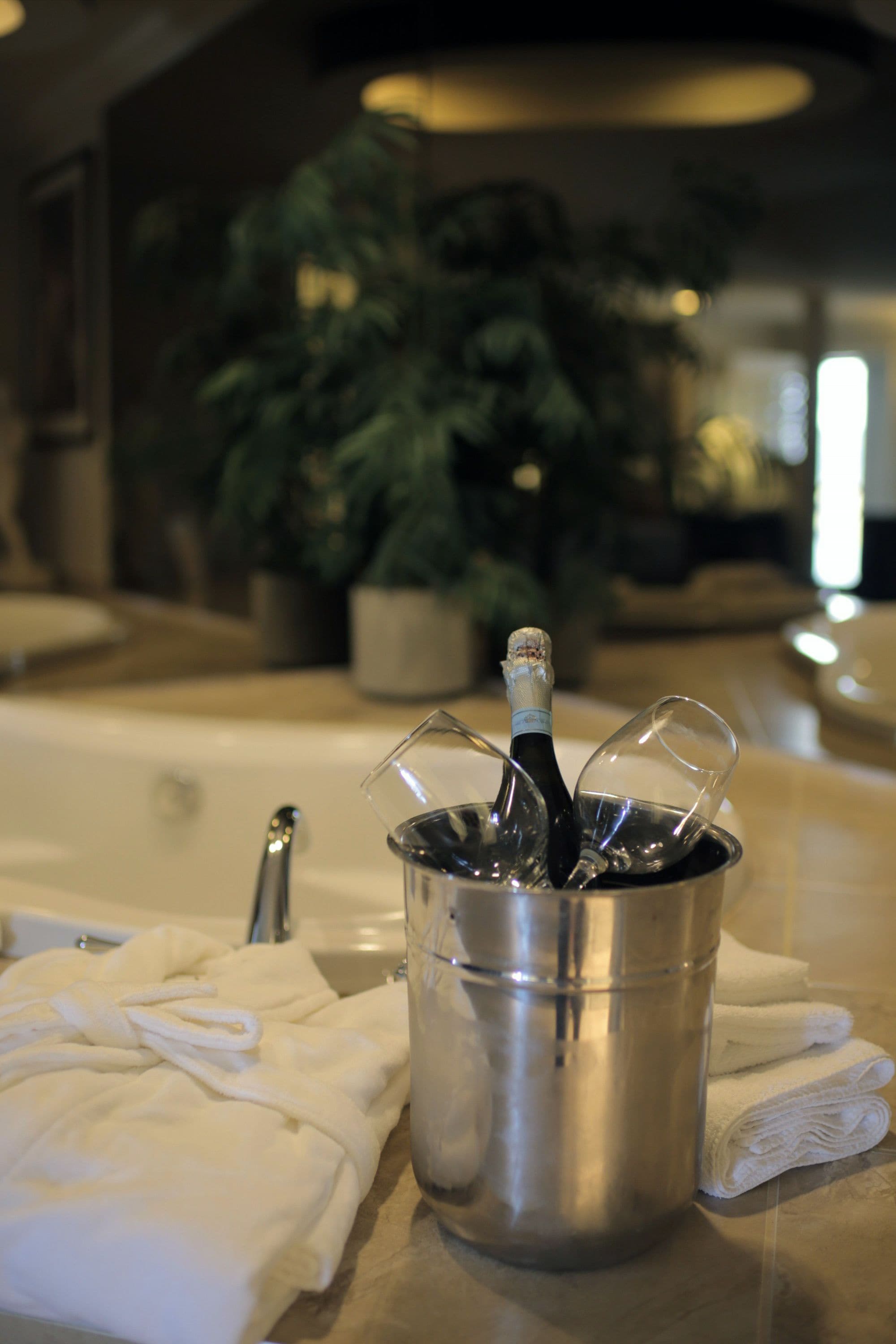 Una bañera con una botella de champán en un balde, rodeada de toallas blancas.