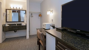 A hotel room with a bathroom vanity, a microwave, a Samsung TV, and a chair.