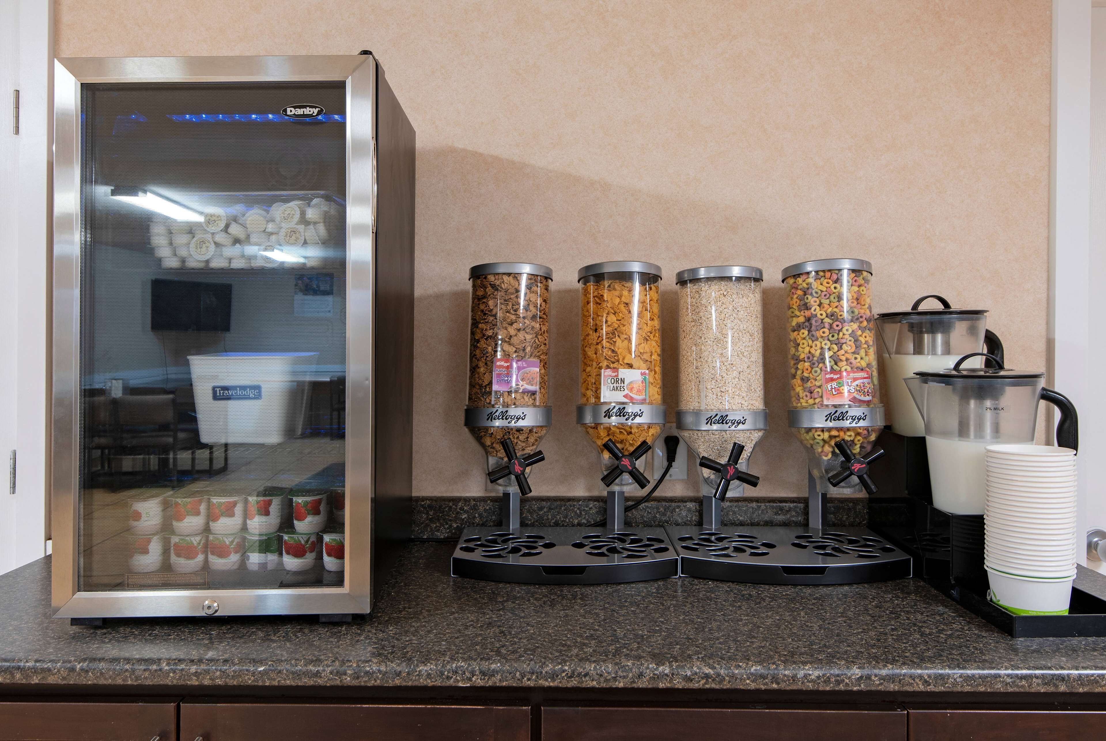 A self-serve beverage station with four dispensers labeled Kellogg's, a refrigerated display case, and a coffee maker.